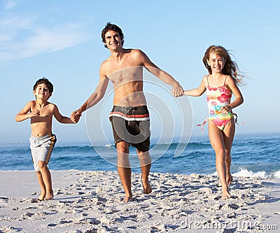 Father Running With Children Along Sandy Beach Stock Photo