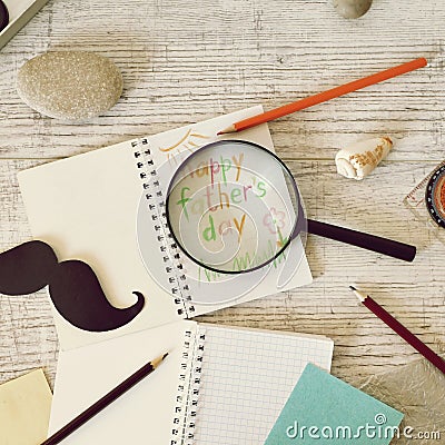 Father`s tools, black paper mustache, magnifying glass, pencils and a greeting inscription in a notebook on a light wooden table Stock Photo