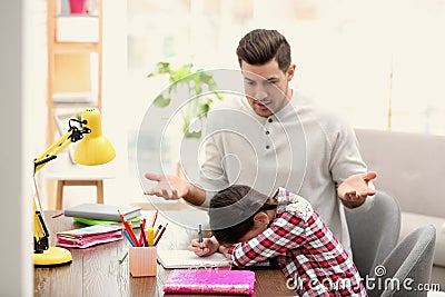 Father scolding his daughter while helping with homework at table Stock Photo