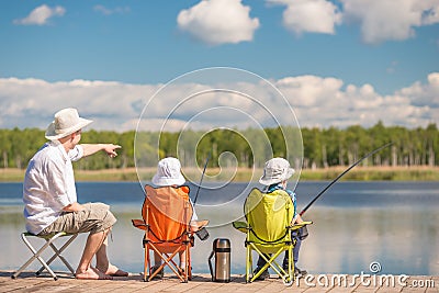 Father shows his children the place of biting fish on the lake, Stock Photo