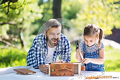 Father with a small daughter outside, making wooden birdhouse. Stock Photo