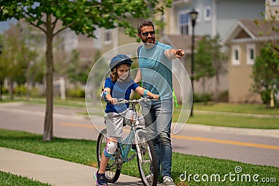 Father and son in bike helmet learning ride bicycle. Father and son on bicycle on summer day outdoor. Little son trying Stock Photo