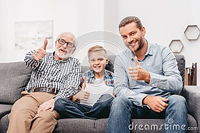 Father, son and grandfather sitting together on couch in living room and showing Stock Photo