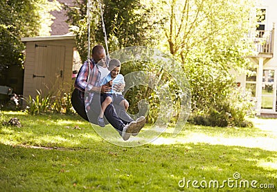 Father And Son Having Fun On Tire Swing In Garden Stock Photo