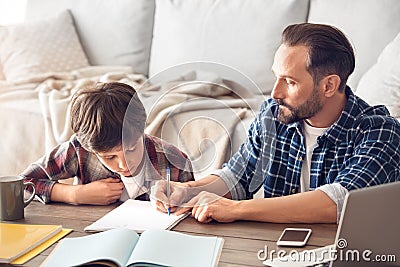 Father and son at home sitting at table showing son to do assignment in notebook serious Stock Photo