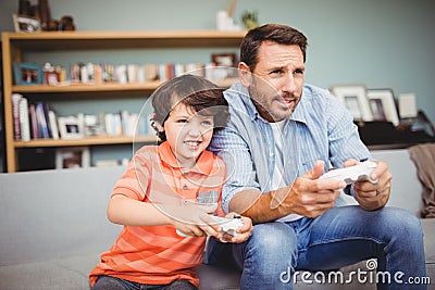 Father and son playing video game while sitting on sofa Stock Photo