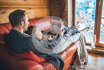 Father and son reading book together lying on the cozy sofa in warm country house. Reading to kids conceptual image Stock Photo