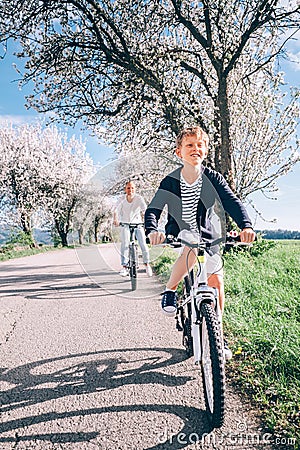 Father with son ride a bicycles on country road under the blossom trees at spring time Stock Photo