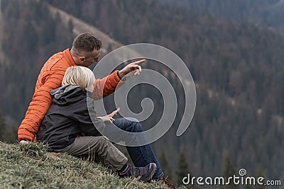 Father and son sit on hillside on the forest background. Trekking and hiking with children. Weekend hike in mountains Stock Photo