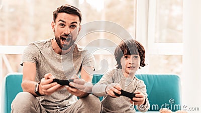 Father and Son Sitting and Playing on Console. Stock Photo