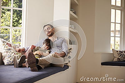 Father And Son Sleeping On Window Seat At Home Together Stock Photo