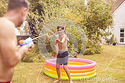 Father And Son Wearing Swimming Costumes Having Water Fight With Water Pistols In Summer Garden Stock Photo