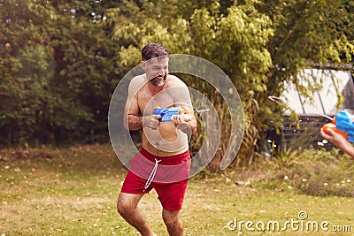 Father And Son Wearing Swimming Costumes Having Water Fight With Water Pistols In Summer Garden Stock Photo