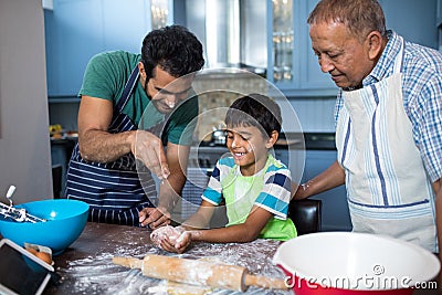 Father sprinkling flour on son hand while preparing food with grandfather Stock Photo