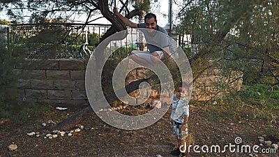 Father squats on the tree to teach kids to play outdoors. Stock Photo