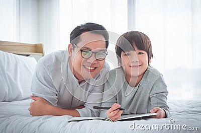 Father teaching his son school homework, lying on the bed with smile for Happy parenting concept Stock Photo