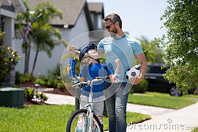 Father teaching son riding bike. Dad helping child son to ride a bicycle in american neighborhood. Child in bike helmet Stock Photo