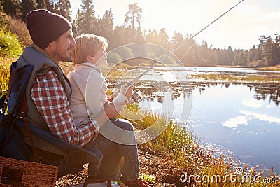 Father teaching son to fish sitting at lakeside Stock Photo