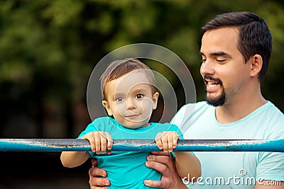 Father teaching toddler son to do pull ups exercise on steel bar outdoors. Healthy family, parental support and sports for kids Stock Photo