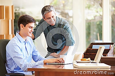 Father And Teenage Son Looking At Laptop Together Stock Photo