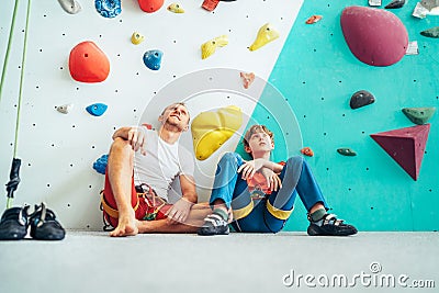 Father and teenage son sitting near the indoor climbing wall. They resting after the active climbing. Happy parenting concept Stock Photo