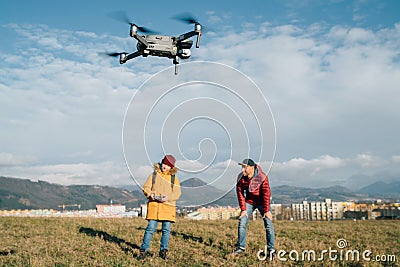 Father and Teenager boy son dressed yellow jacket piloting a modern digital drone using remote controller. Modern technology Stock Photo