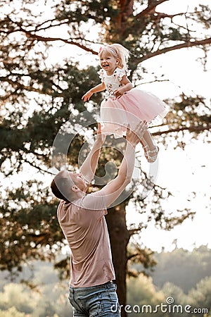 Father throws baby in nature, girl flies in the sky. Portrait dad with child together. Daddy, little daughter outdoors Stock Photo