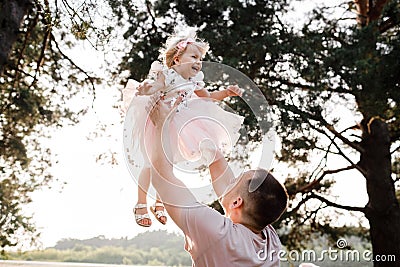 Father throws baby in nature, girl flies in the sky. Portrait dad with child together. Daddy, little daughter outdoors Stock Photo