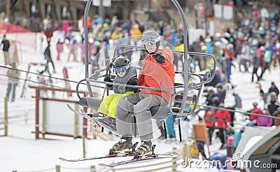Father & Toddler Son On a Ski Lift at a Colorado Mountain Resort with Crowds of People in the Background. Waving & Smiling. Stock Photo