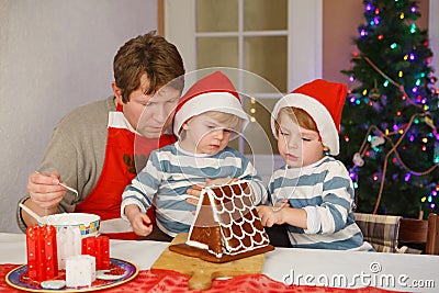 Father and two little sons decorating a gingerbread cookie house Stock Photo