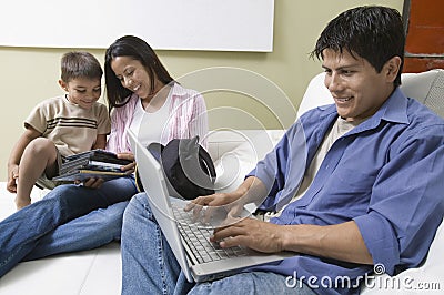 Father Using Laptop, mother and son Looking at DVD Stock Photo