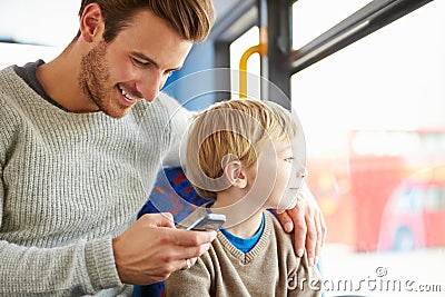 Father Using Mobile Phone On Bus Journey With Son Stock Photo