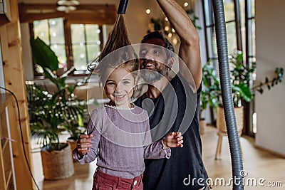 Father vacuuming girl's hair with vacuum cleaner. Father and daughter cleaning the house, helping with house chores. Stock Photo