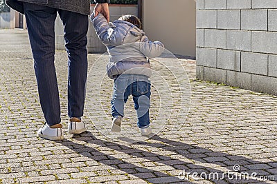 A father walks holding the little daughter tenderly by the hand to help her learn to walk Stock Photo