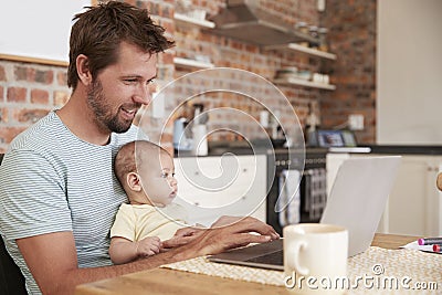 Father Working From Home On Laptop With Baby Son Stock Photo