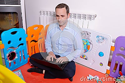 Father working with laptop inside baby playground to take care of his son Stock Photo