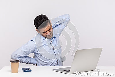 Fatigued businessman sitting office workplace with laptop, feeling exhausted with sore back, massaging stiff muscles Stock Photo