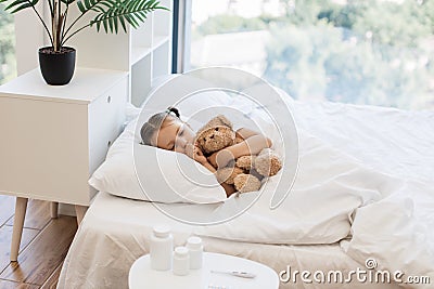 Fatigued cute girl hugging toy bear and coughing in bed Stock Photo