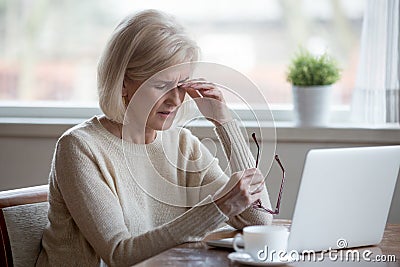 Fatigued mature woman taking off glasses suffering from eye stra Stock Photo