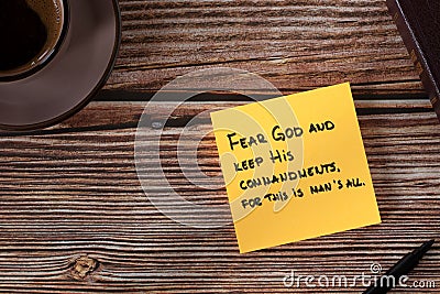 Fear God and keep His commandments, handwritten verse on yellow note with bible book and coffee cup on wooden table, top view Stock Photo