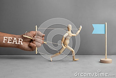 Fear of obstacles on the way to the goal. Fear as puppeteer holds doll and does not let him go to the flag as symbol of the goal Stock Photo