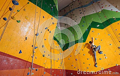 Fearless woman climbing up the orange wall in gym Stock Photo