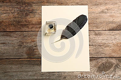 Feather pen, inkwell and blank parchment on wooden table, top view Stock Photo