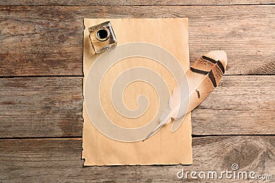 Feather pen, inkwell and blank parchment on wooden table, top view Stock Photo