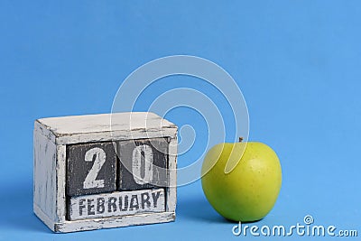 February 20th on wooden calendar and green apple on blue background. Apple Day USA. Stock Photo