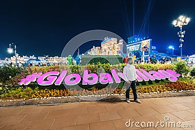 Tourist visitor takes a photo against the background of the glowing inscription Global Village Editorial Stock Photo