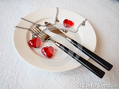 February 14 is Valentine`s Day, a holiday for all lovers. Still life of a white plate, knife, fork, three red hearts, two togethe Stock Photo