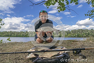 Feeder fishing. Fisherman with vimba bream fish in hands and tackle at wild river shore Stock Photo
