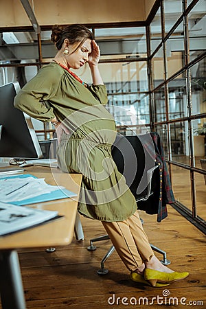 Pregnant businesswoman wearing yellow shoes feeling awful at work Stock Photo