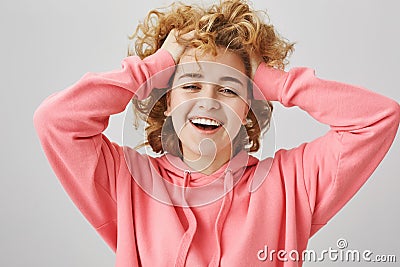 Feeling carefree and happy. Portrait of emotive young woman with curls, pulling hair backwards with hands, smiling Stock Photo